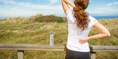 Woman stretching outdoors near a bench with a water bottle.