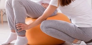 Person assisting another with leg stretch using an exercise ball.