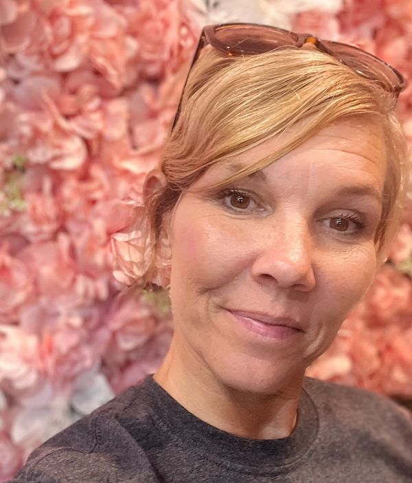 A woman smiling with a floral pink background.