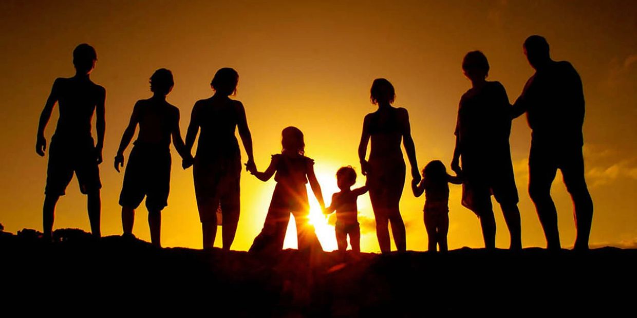 Silhouetted family holding hands at sunset.