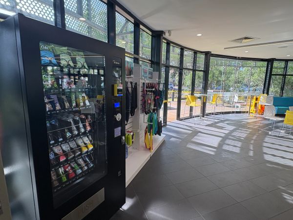 Modern vending machine in a bright, spacious lounge with large windows and yellow chairs.