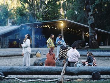 Group of people gathered outdoors near a fire pit with string lights.