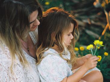 A woman and a girl holding yellow flowers outdoors.