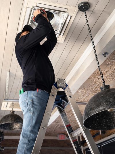 A man on a ladder fixing a ceiling light fixture.