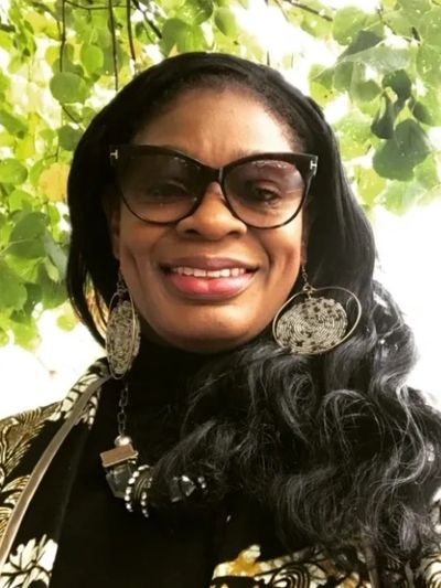 Woman smiling outdoors wearing large sunglasses and statement earrings.