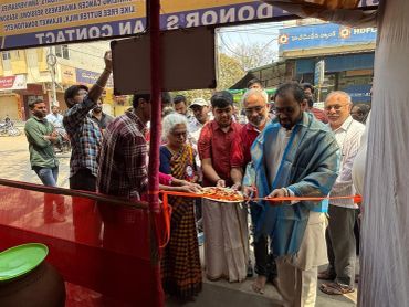 Man cutting a ribbon at an inauguration ceremony with people watching.