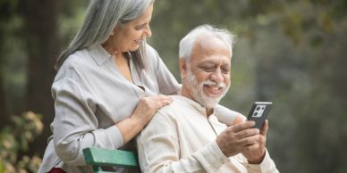 Elderly couple smiling at a smartphone outdoors.