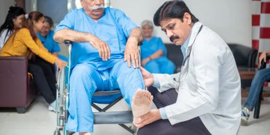 Doctor examining elderly man's leg in a clinic waiting room.
