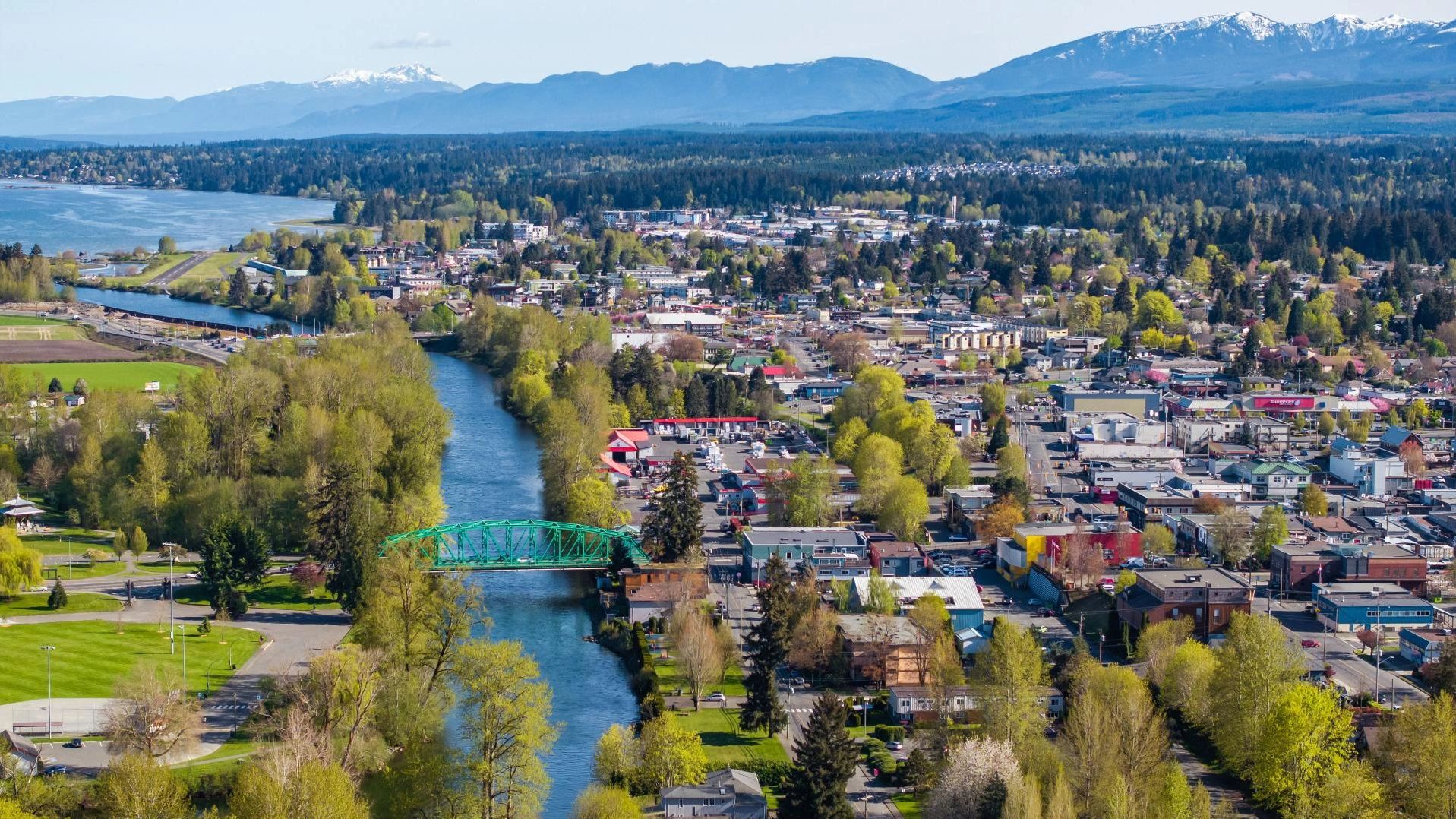 A scenic town with a river, green bridge, and mountains in the background.