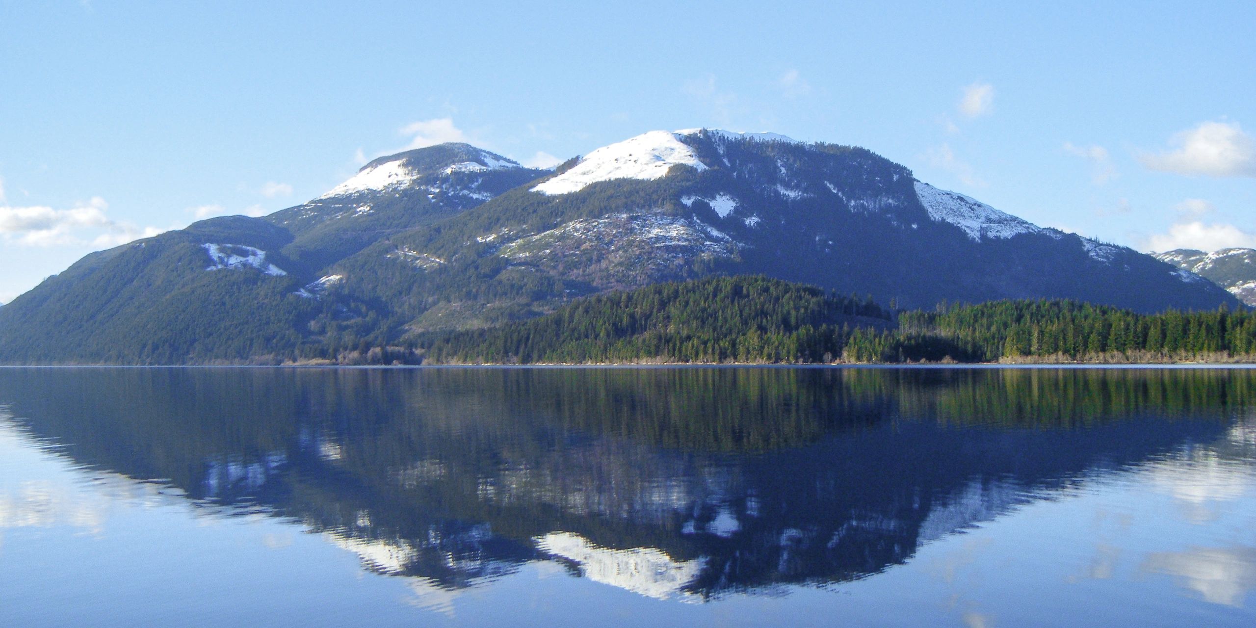 Snow-capped mountains reflecting on a calm lake under a clear blue sky.