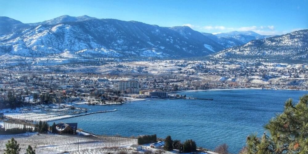 Snowy town by a large blue lake surrounded by mountains.