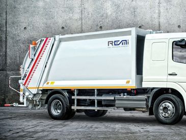 White garbage truck parked against a concrete wall.