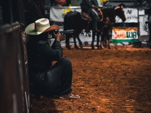 Person with cowboy hat taking photo at rodeo.