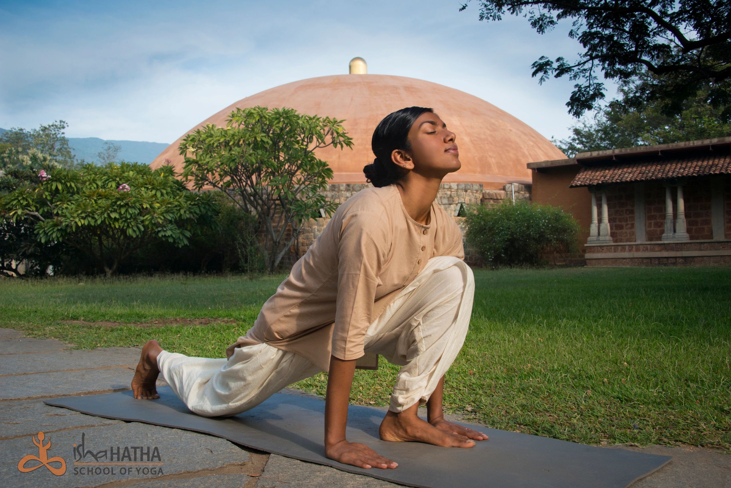 A woman practicing yoga outdoors in front of a dome-shaped structure.