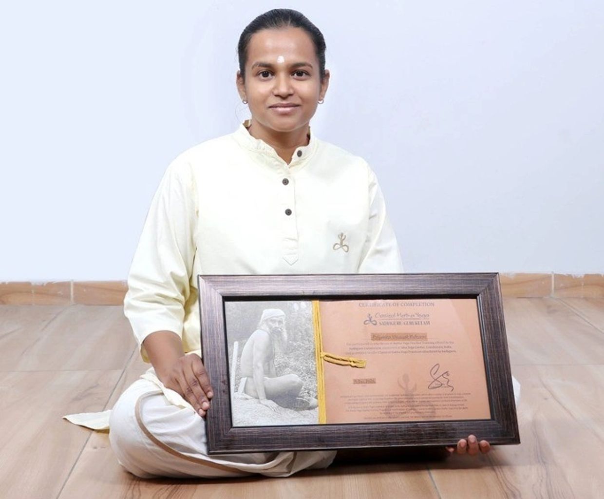 Person in traditional attire holding a framed certificate with a photo and text.