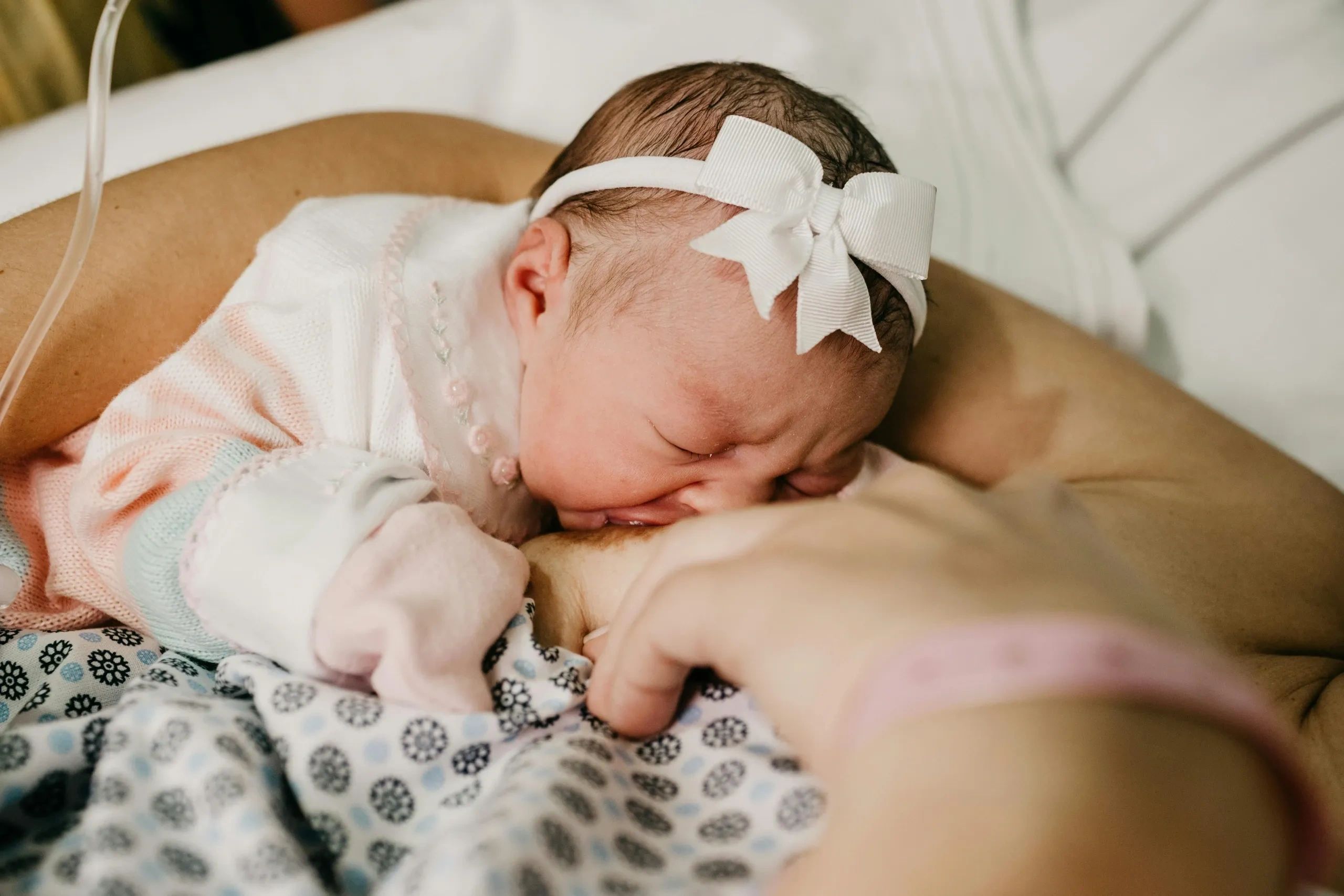 infant with light skin wearing a white bow on their head while latched to a light skinned breast