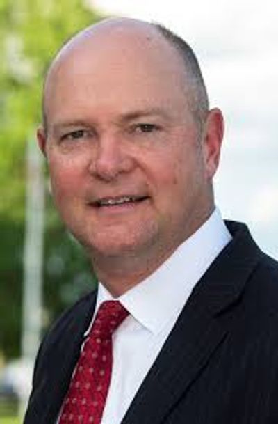 A professional man in a suit and red tie smiling outdoors.
