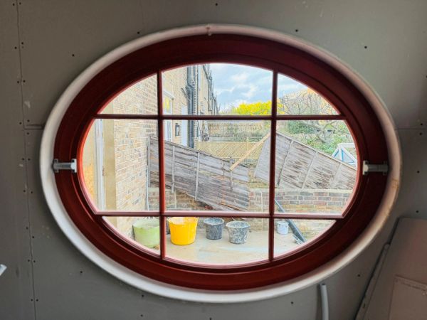 View through a round window showing a patio with buckets and a fence.