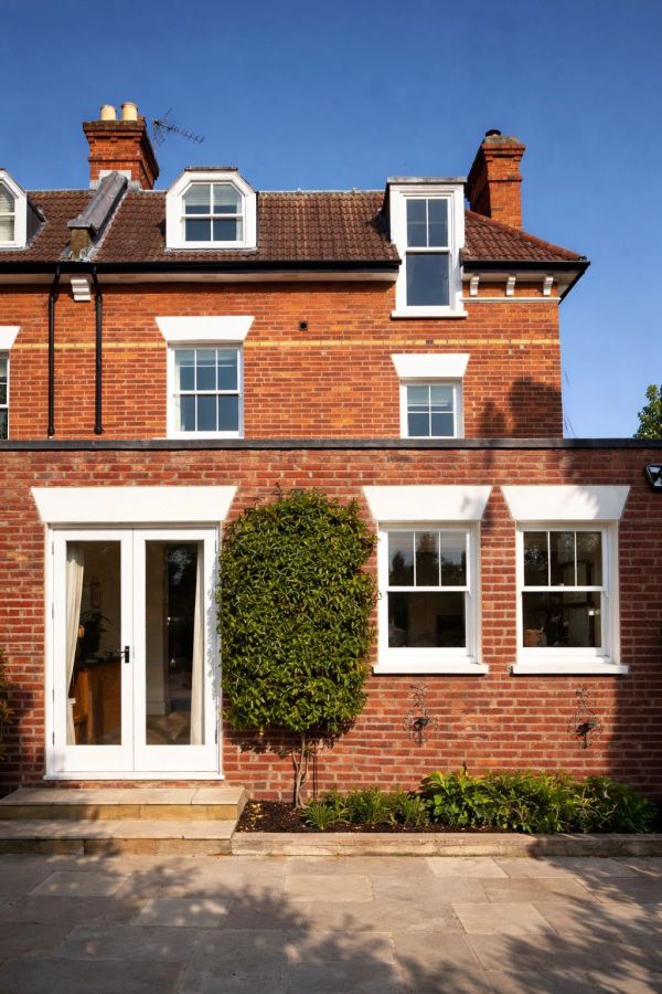 Brick house with white-framed windows and a small garden under a clear blue sky.