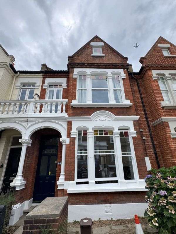 Red brick townhouse with white window frames and a dark blue door under a cloudy sky.