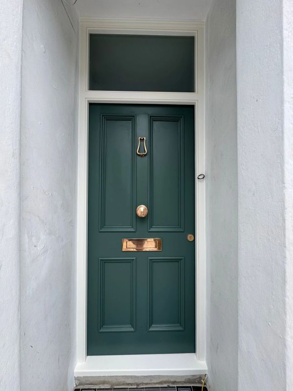 Dark green front door with gold hardware in white entrance.