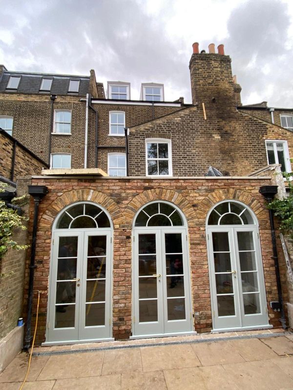 Three arched French doors on a brick extension with a cloudy sky.
