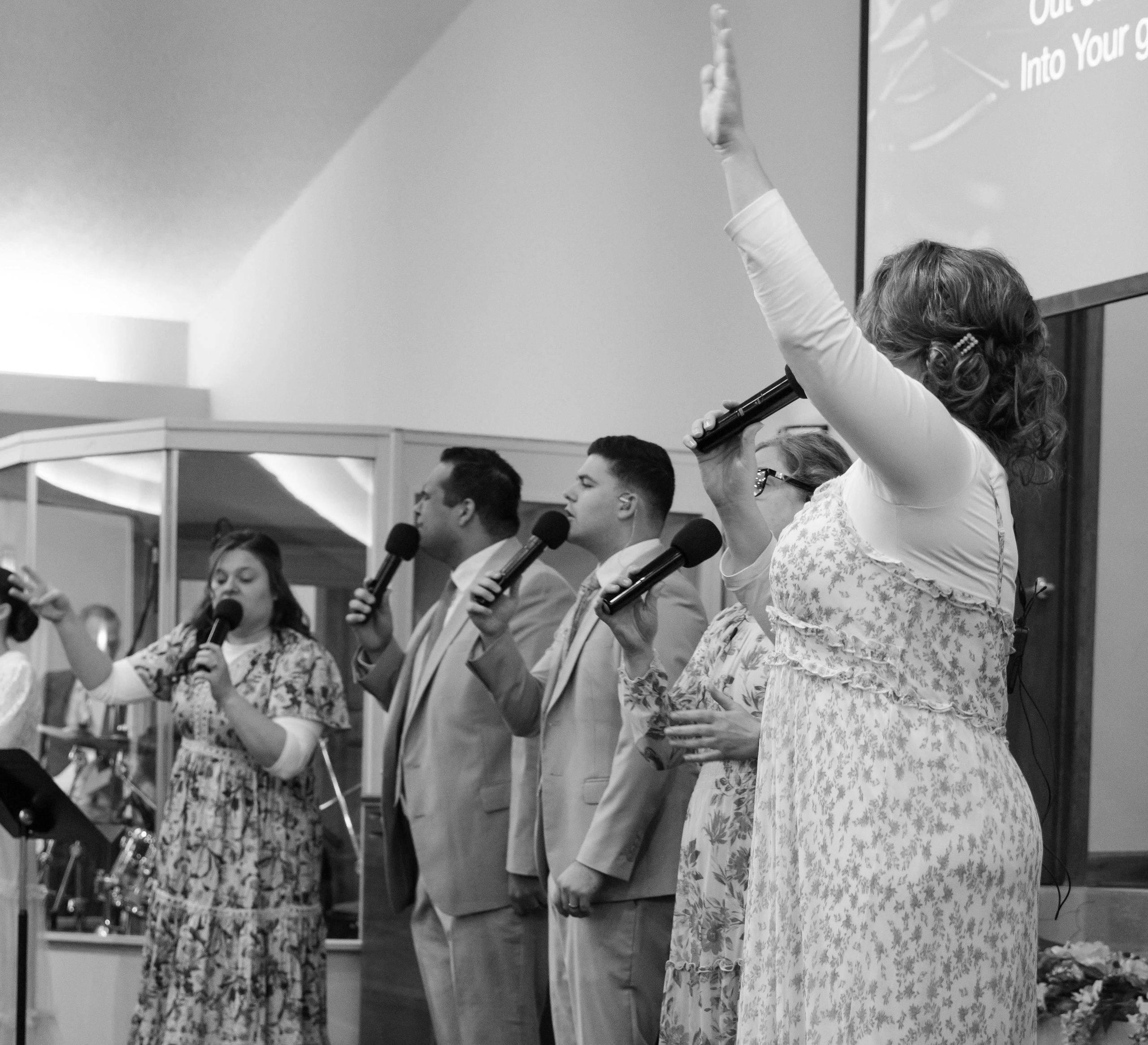 A group singing on stage with raised hands and microphones.