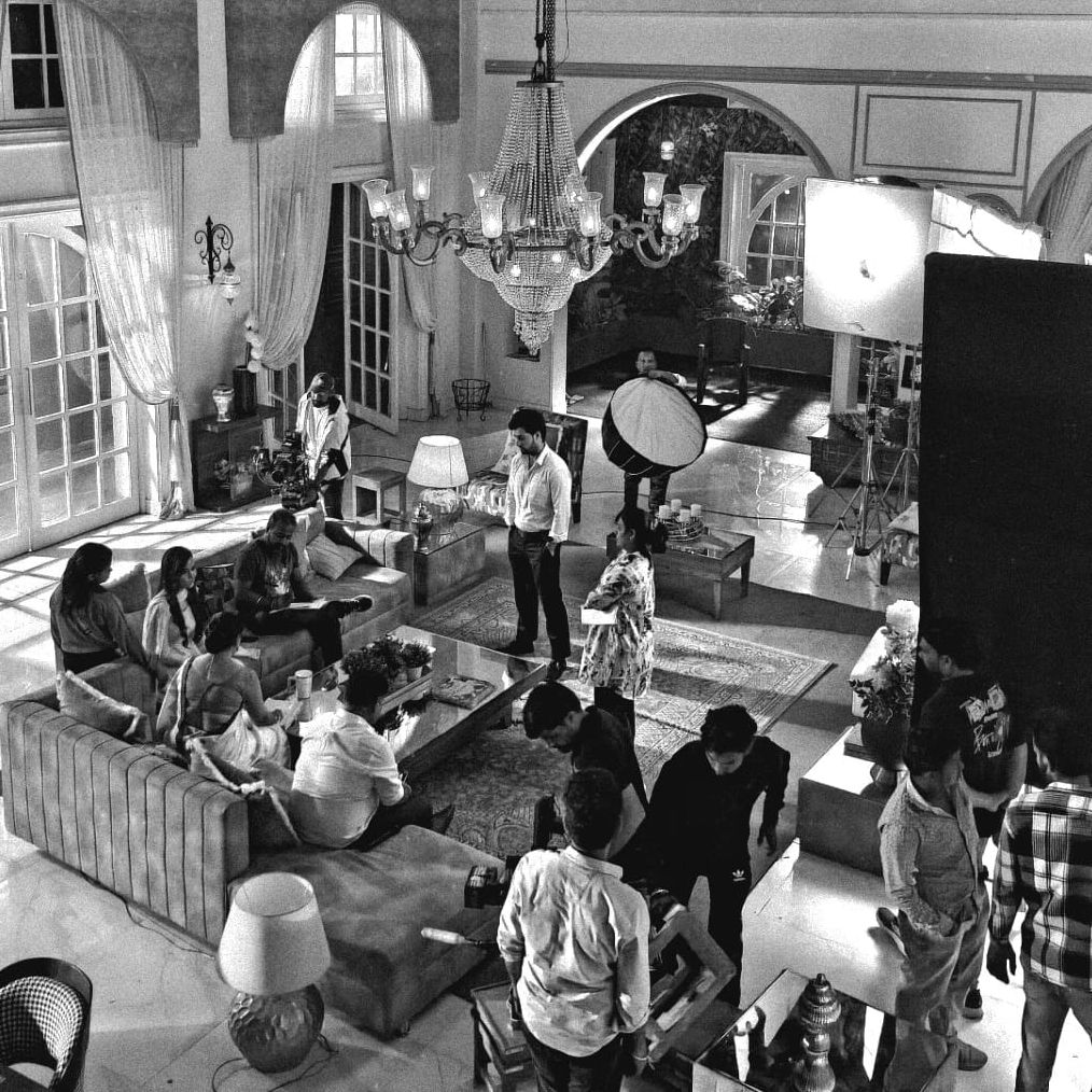 A busy film set inside an elegant living room with crew and actors.