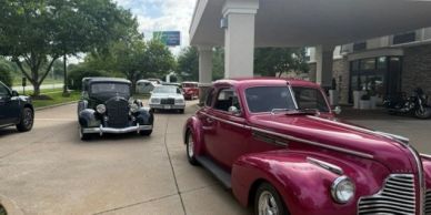 Line of vintage cars on a driveway near a building.
