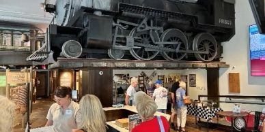 A vintage train engine displayed indoors over a restaurant area.