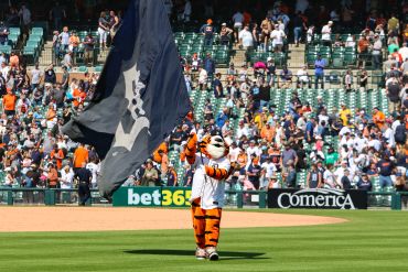 Detroit Tigers mascot waving a large flag on the baseball field during a game.