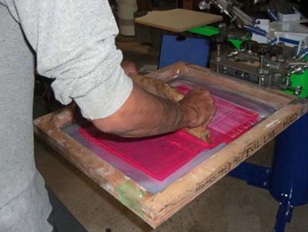 A printer pulls a squeegee over a screen