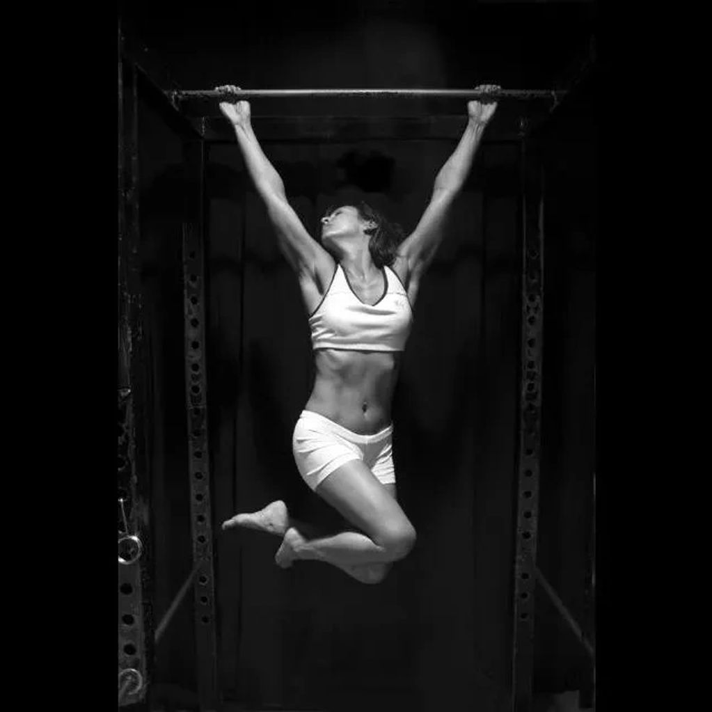 Woman performing pull-up exercise on a bar in black and white.