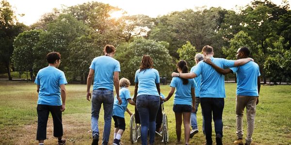 Group of diverse people walking together outdoors, supporting a person in a wheelchair.