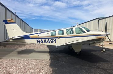 Small single-engine airplane parked beside hangars under a partly cloudy sky.
