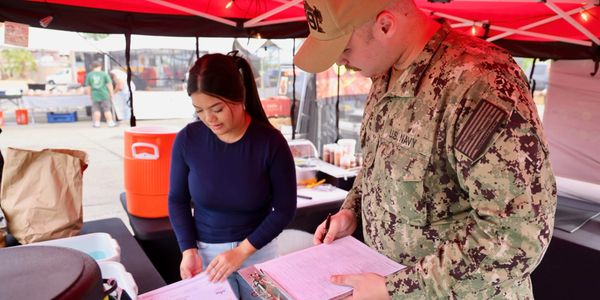 A woman and a Navy member reviewing documents under a red canopy.