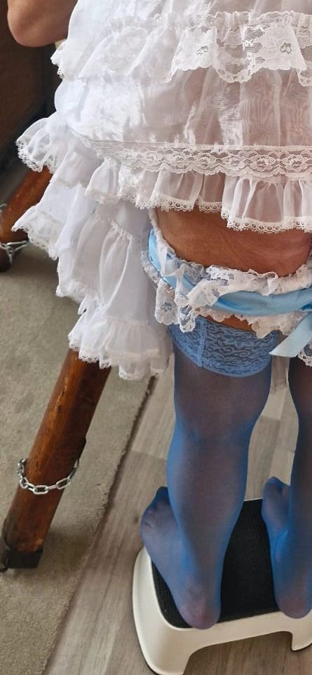 Person wearing white lace dress and blue stockings standing on a step stool.