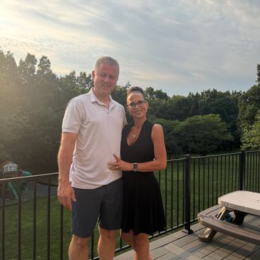 Couple standing on a deck outdoors at sunset.