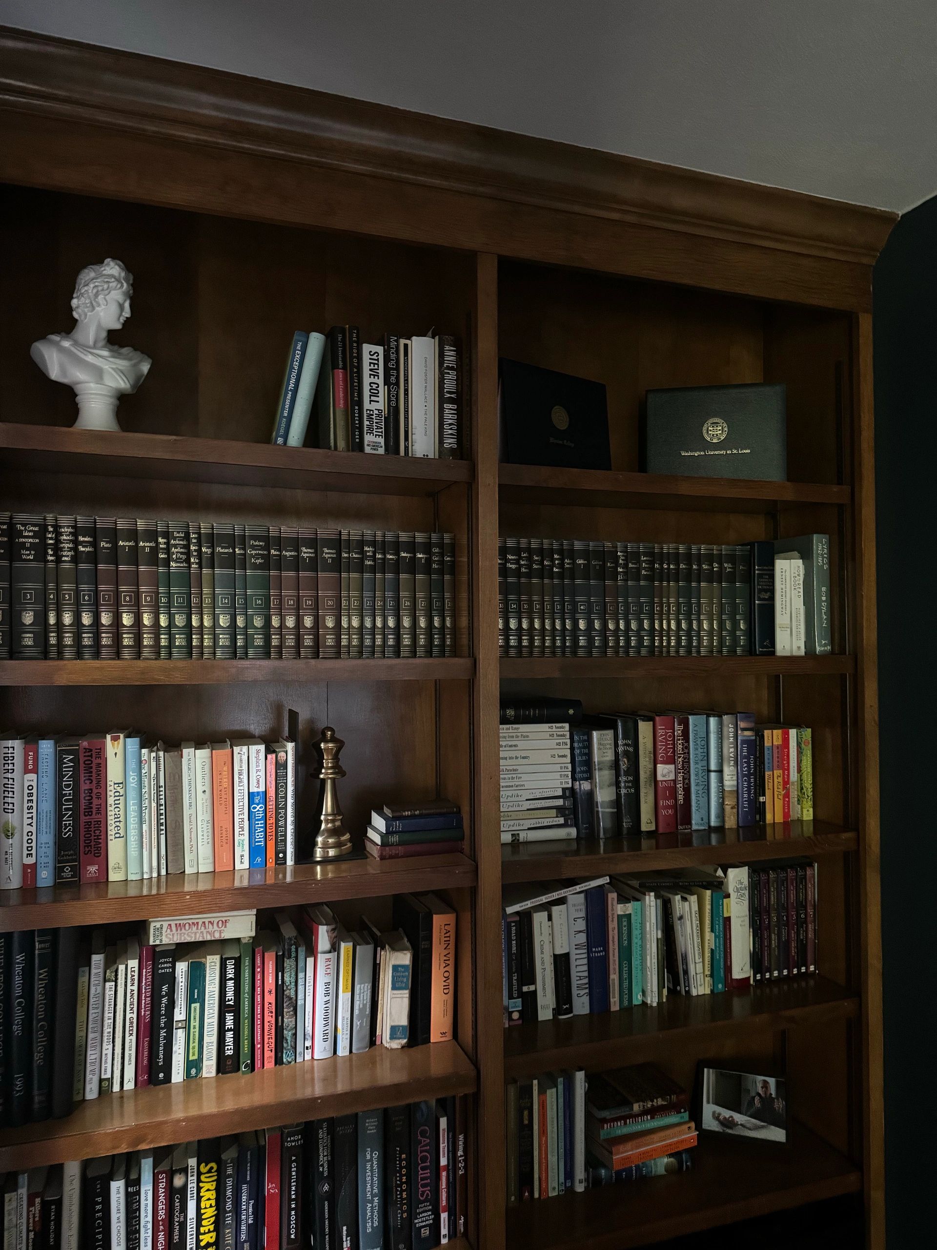 Wooden bookshelf filled with books, a chess piece, and a bust statue.