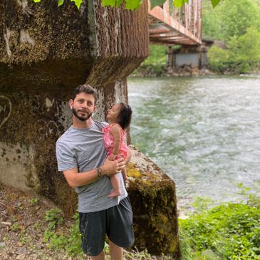 A grandpa and his granddaughter standing in front of a river