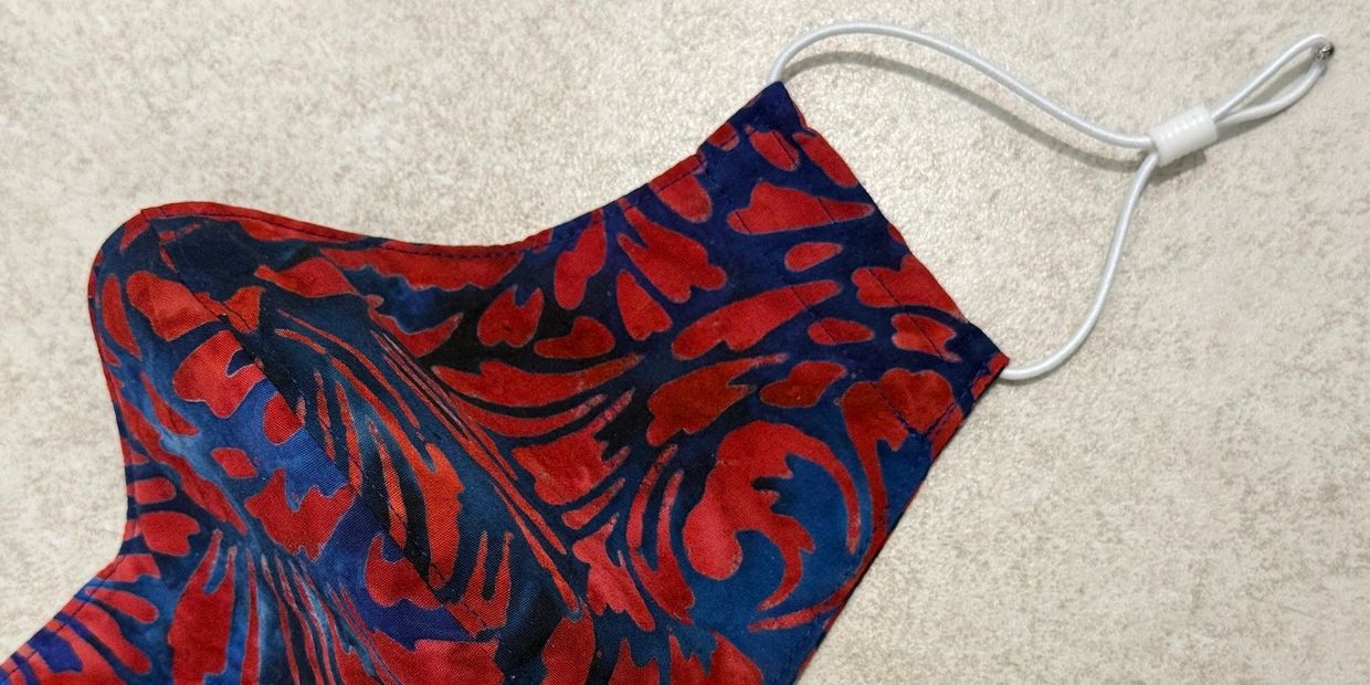 Fabric face mask with red and blue floral pattern and adjustable white ear loops.