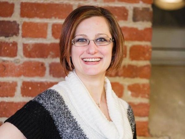 Smiling woman with glasses wearing a black, white, and gray sweater.