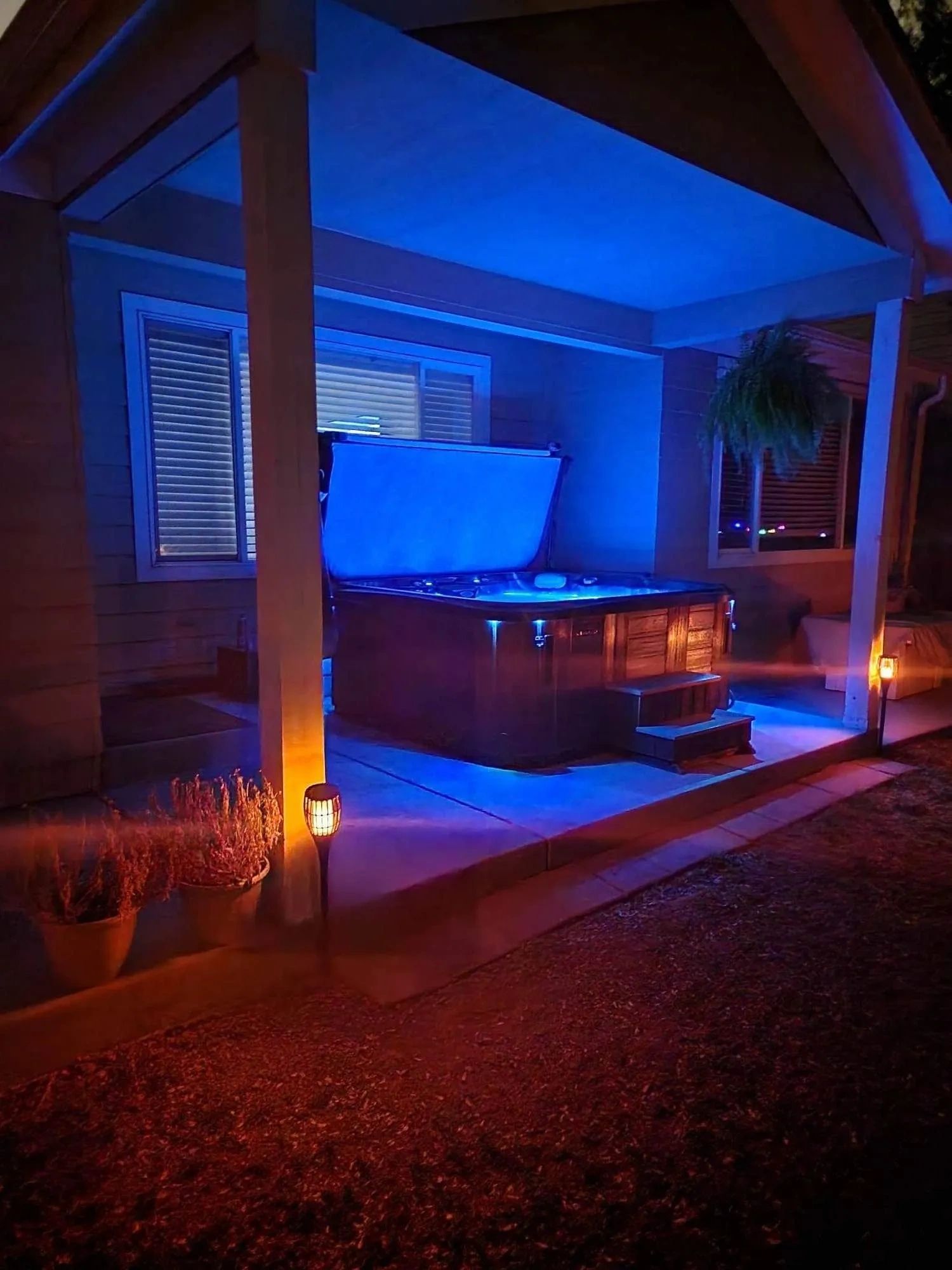 A backyard hot tub glowing with blue lights under a covered patio at night.