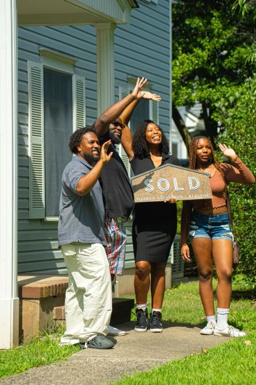 Happy family waving outside their new home with a sold sign.