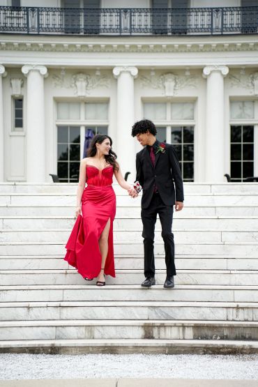 Couple walking down elegant white stairs, dressed formally and holding hands.