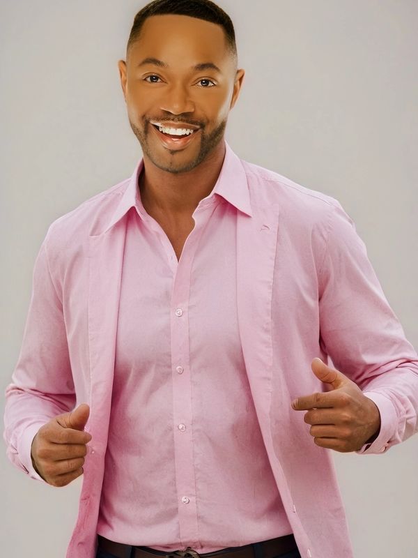 Smiling man in a pink shirt and blazer poses confidently.