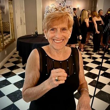 Elderly woman smiling with a tiara in a black dress.