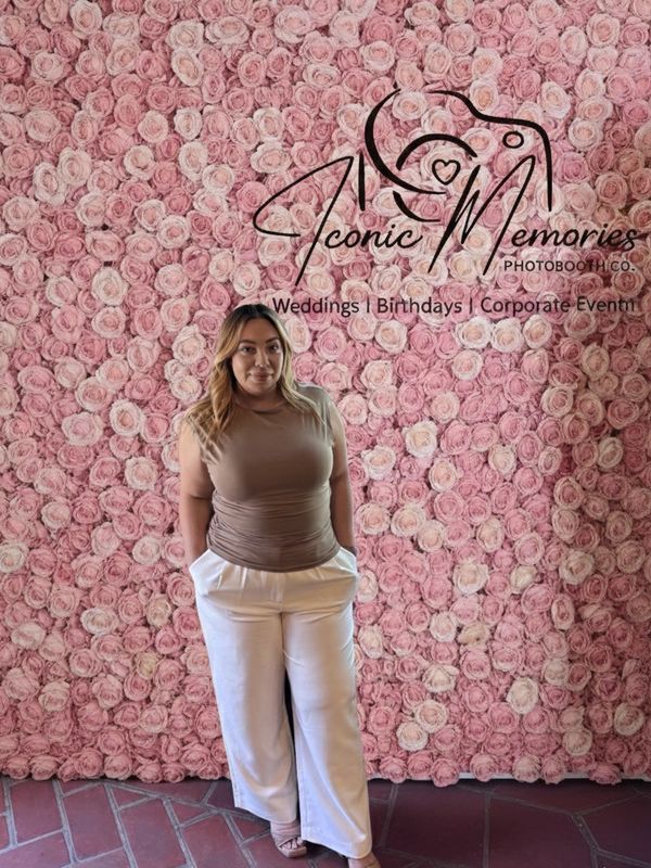 Woman posing in front of a pink rose wall with event photography logo.