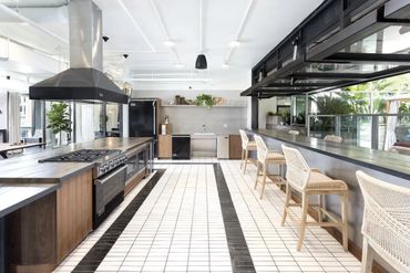 Modern kitchen with wooden cabinets, white tiled floor, and bar seating.