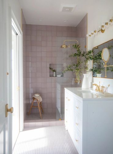 Bright bathroom with pink tiles, gold fixtures, and a wooden stool in the shower.
